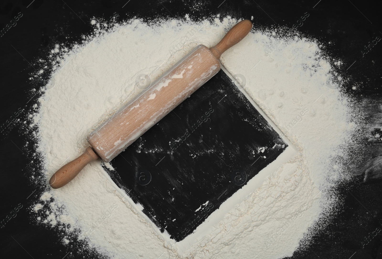 Photo of Flour and rolling pin on black table, top view. Space for text