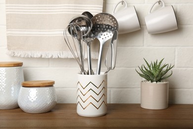 Steel utensils and different dishware on wooden table near white brick wall in kitchen