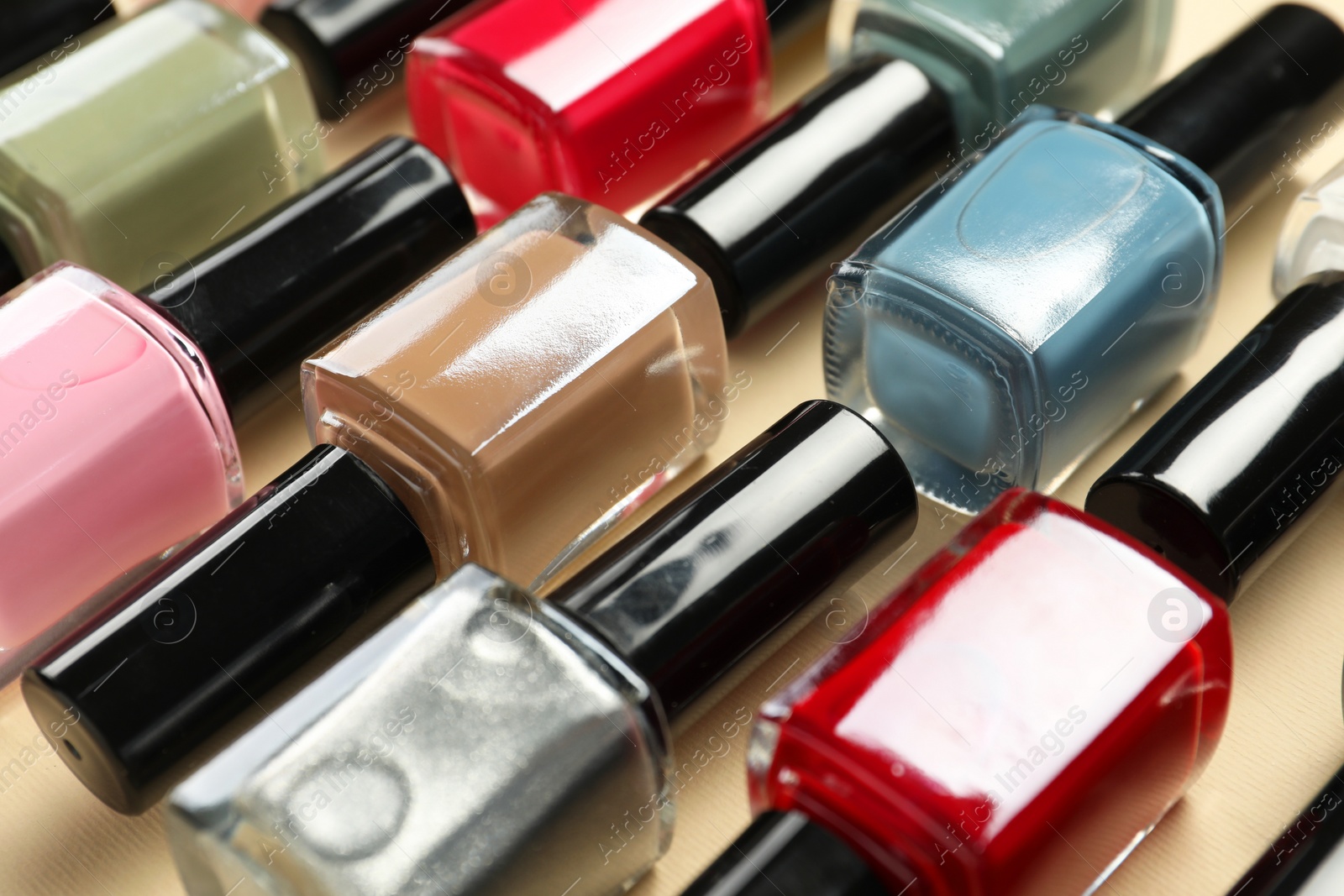 Photo of Bright nail polishes in bottles on beige background, closeup