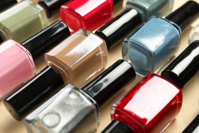 Photo of Bright nail polishes in bottles on beige background, closeup