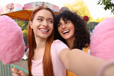 Happy friends with cotton candies taking selfie at funfair
