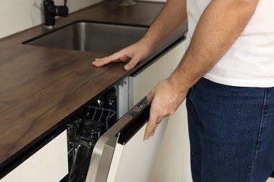 Photo of Man opening dishwasher's door in kitchen, closeup
