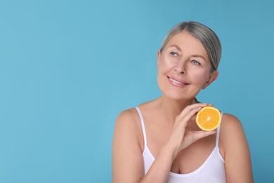 Photo of Beautiful woman with half of orange rich in vitamin C on light blue background, space for text