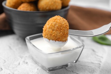 Photo of Dipping fried tofu ball into sauce on white textured table, closeup