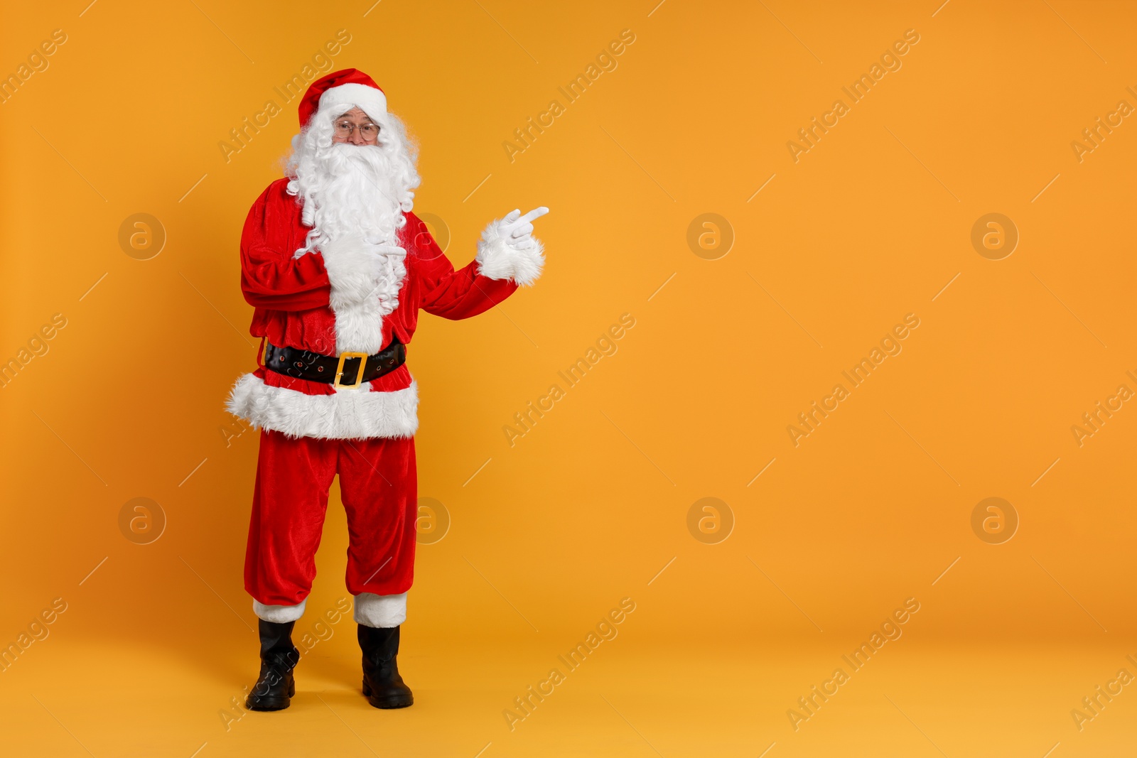 Photo of Merry Christmas. Santa Claus pointing at something on orange background, space for text