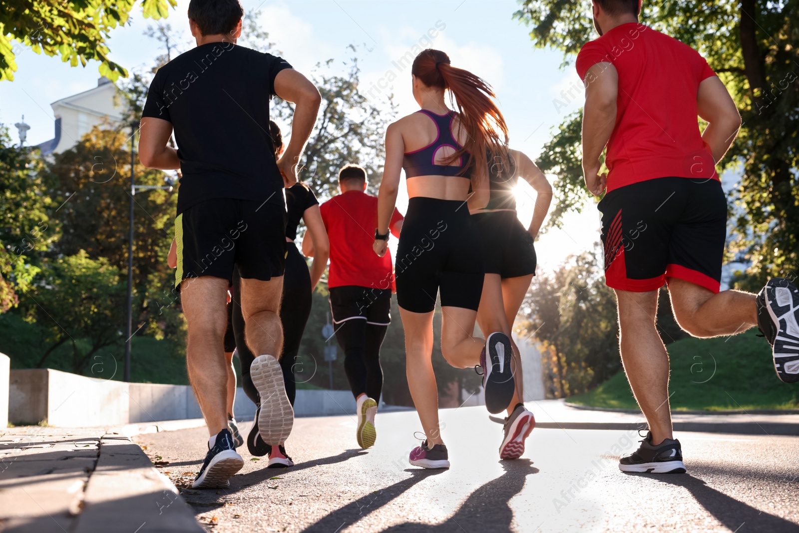 Photo of Group of people running outdoors on sunny day, back view