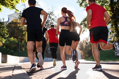 Photo of Group of people running outdoors on sunny day, back view