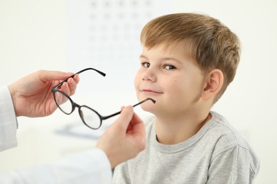 Photo of Vision testing. Ophthalmologist giving glasses to little boy indoors