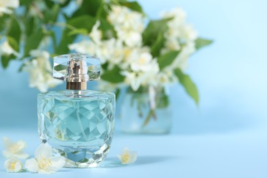 Aromatic perfume in bottle and beautiful jasmine flowers on light blue background, closeup. Space for text