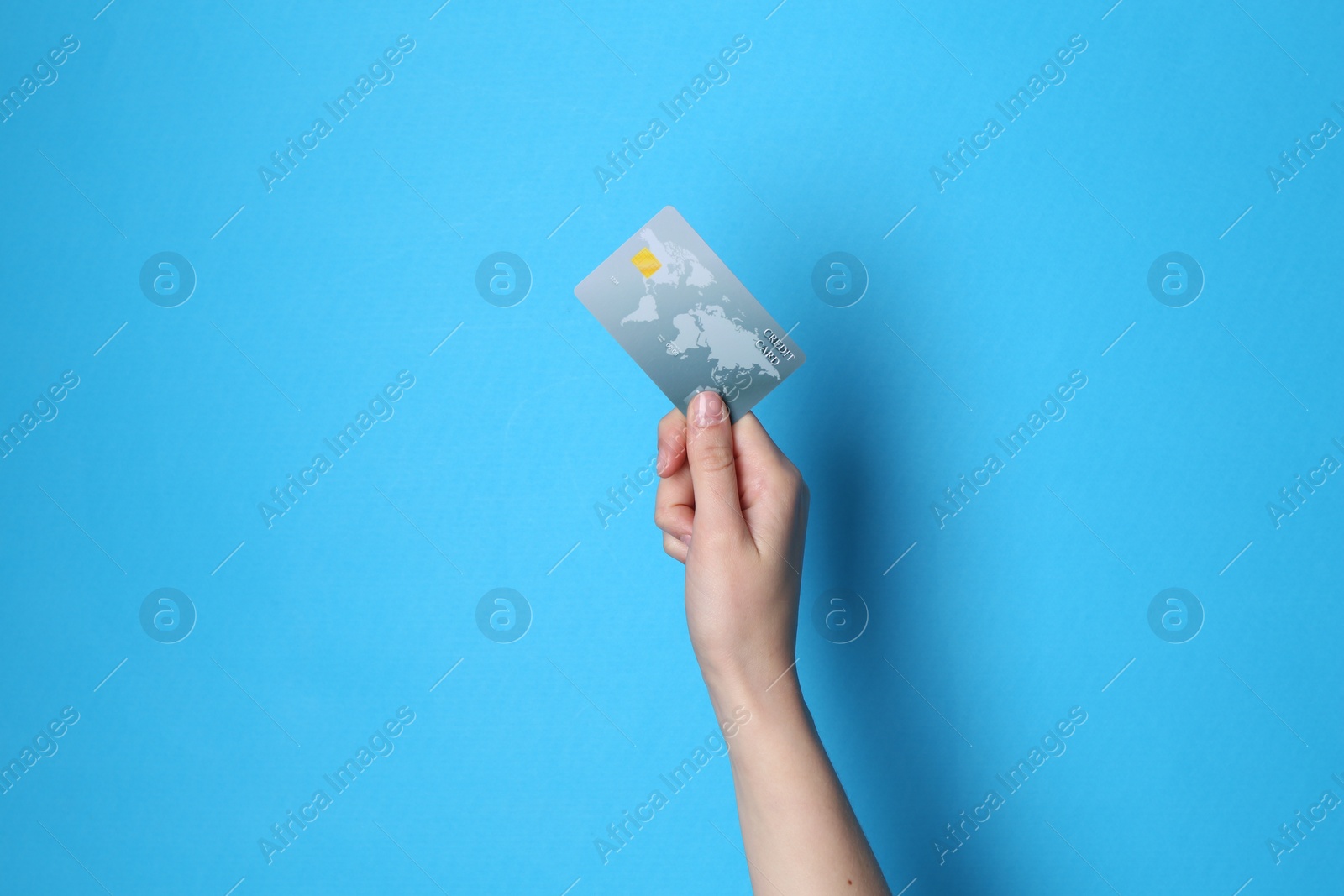 Photo of Woman holding credit card on light blue background, closeup