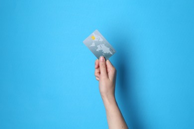 Woman holding credit card on light blue background, closeup