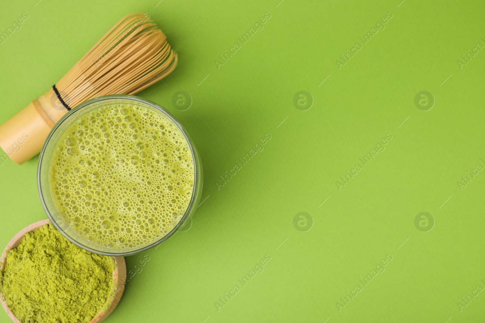 Photo of Glass of tasty matcha smoothie, powder and bamboo whisk on green background, flat lay. Space for text