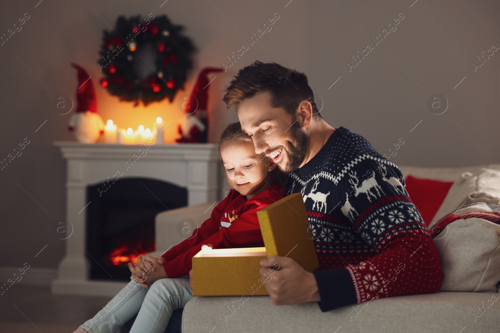 Photo of Father and his cute daughter opening gift box with magical light at home. Christmas celebration