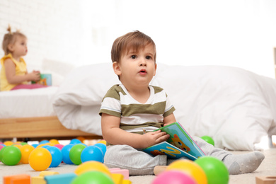 Cute little boy with book playing on floor while girl sitting on bed. Children's development