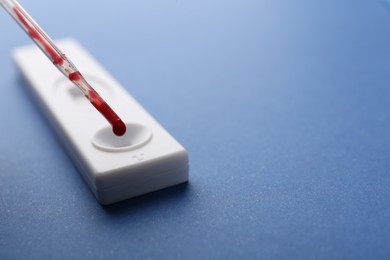 Photo of Dropping blood sample onto disposable express test cassette with pipette on blue background, closeup. Space for text