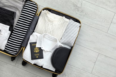 Photo of Open suitcase with clothes and passport on floor, top view. Space for text