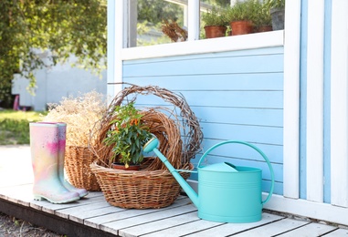 Rubber boots, watering can, baskets and plant near house outdoors. Gardening tools