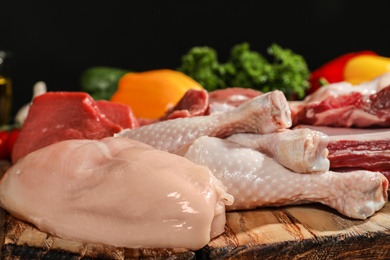 Wooden board with fresh raw meat on table against dark background