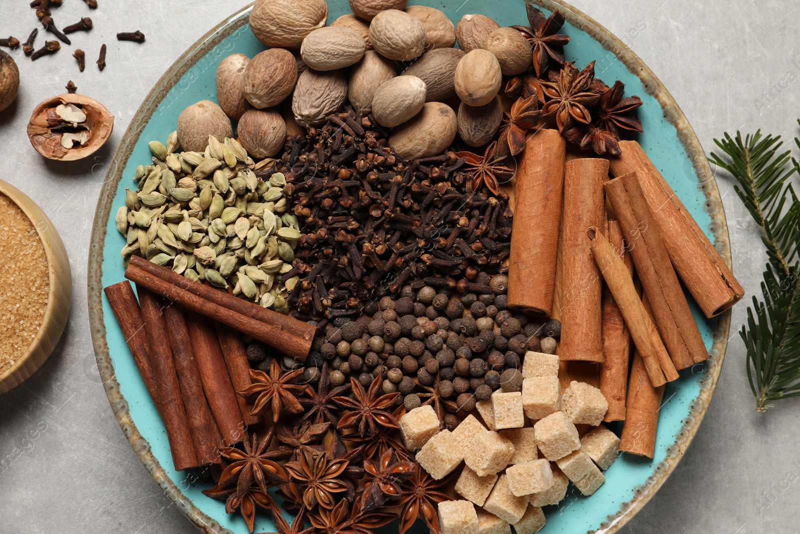 Photo of Different spices with nuts in bowls and fir branch on light gray textured table, flat lay