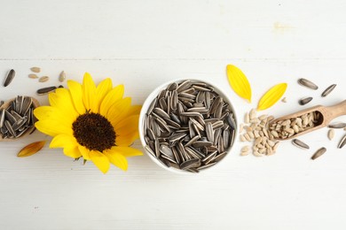 Photo of Organic sunflower seeds, scoop and bright flower on white wooden table, flat lay