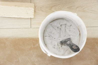 Photo of Bucket with plaster and putty knife on floor indoors, top view. Space for text