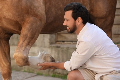 Photo of Man examining horse leg outdoors. Pet care
