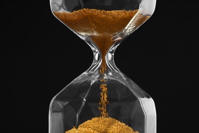 Photo of Hourglass with flowing sand on dark brown background, closeup