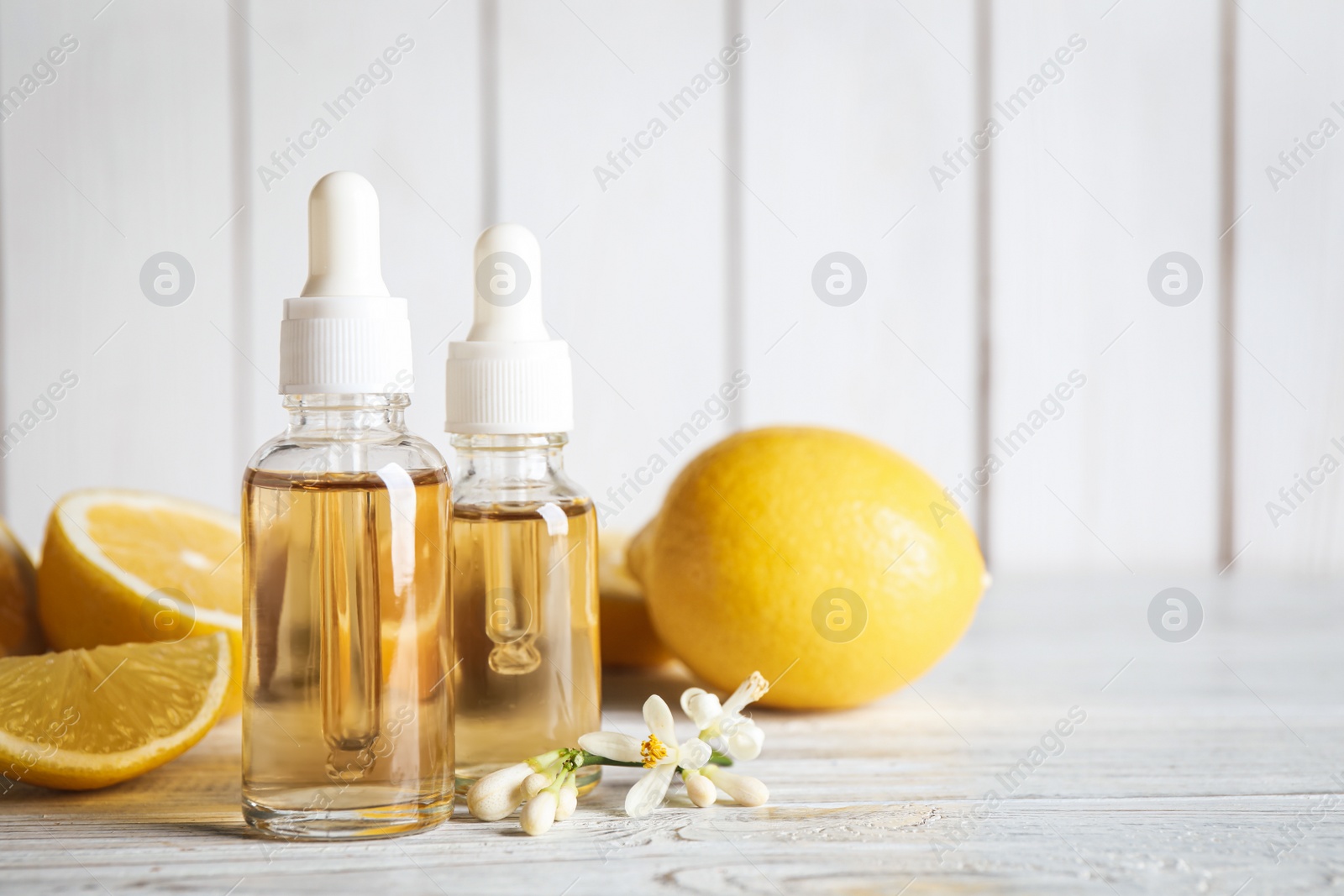 Photo of Bottles of citrus essential oil, flower and lemons on white wooden table. Space for text