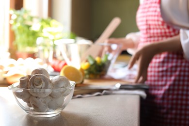 Photo of Woman preparing salad in kitchen, focus on bowl with mushrooms