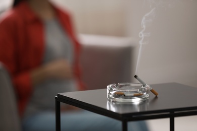 Photo of Cigarettes in ash tray and blurred pregnant woman on background, closeup. Space for text