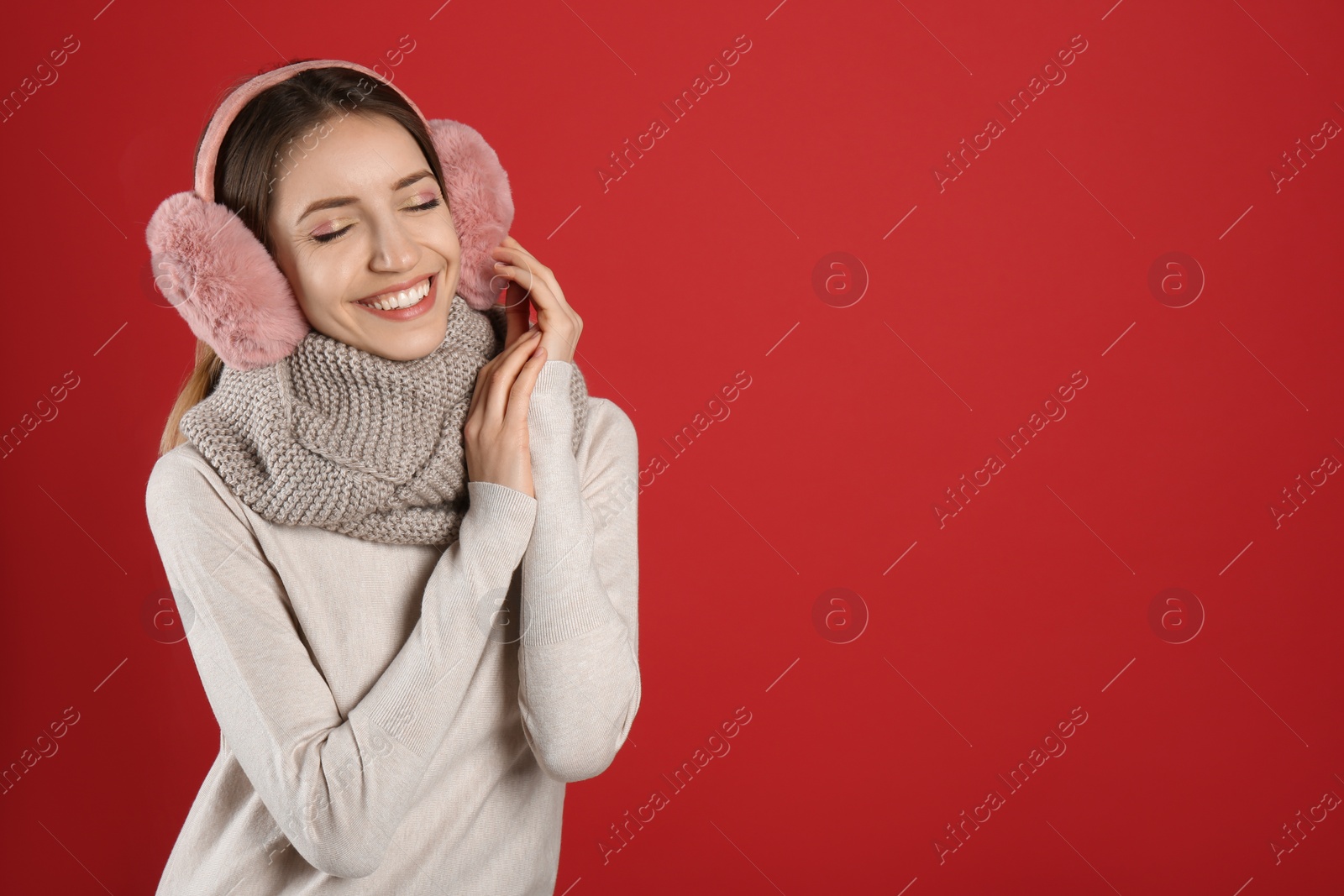 Photo of Happy woman wearing warm earmuffs on red background, space for text