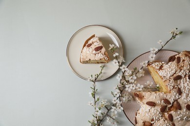 Photo of Plates with cut delicious Italian Easter dove cake (traditional Colomba di Pasqua) and flowering branches on light grey table, flat lay. Space for text