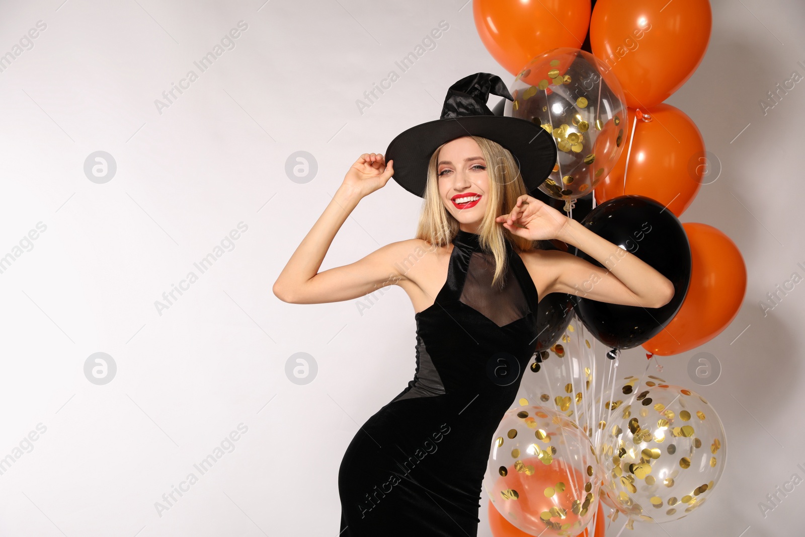 Photo of Beautiful woman in witch costume with balloons on white background, space for text. Halloween party