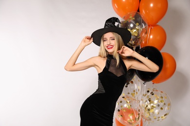 Photo of Beautiful woman in witch costume with balloons on white background, space for text. Halloween party