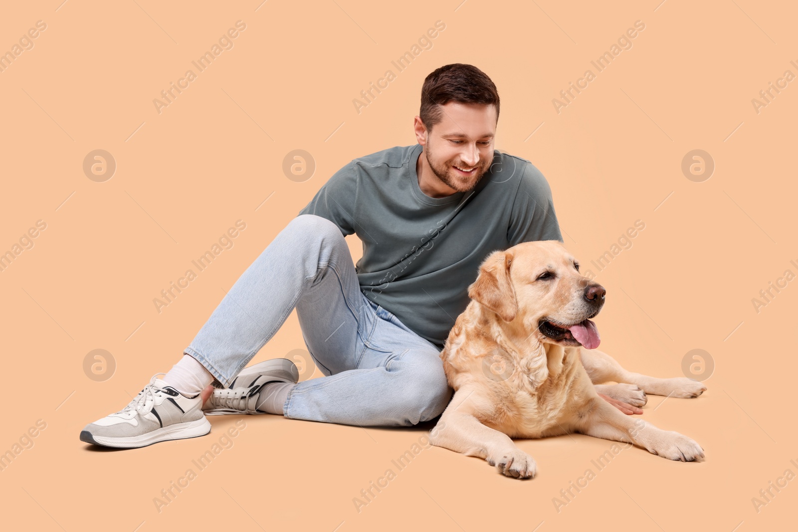 Photo of Man with adorable Labrador Retriever dog on beige background. Lovely pet