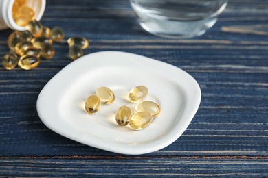 Plate with cod liver oil pills on wooden background, closeup