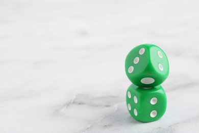 Two green game dices on white marble table, closeup. Space for text