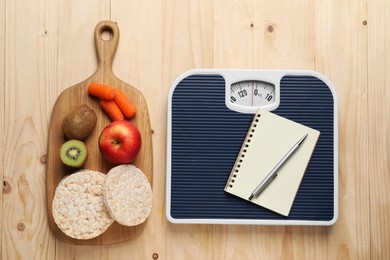 Photo of Healthy diet. Scale with notebook and products on wooden table, flat lay