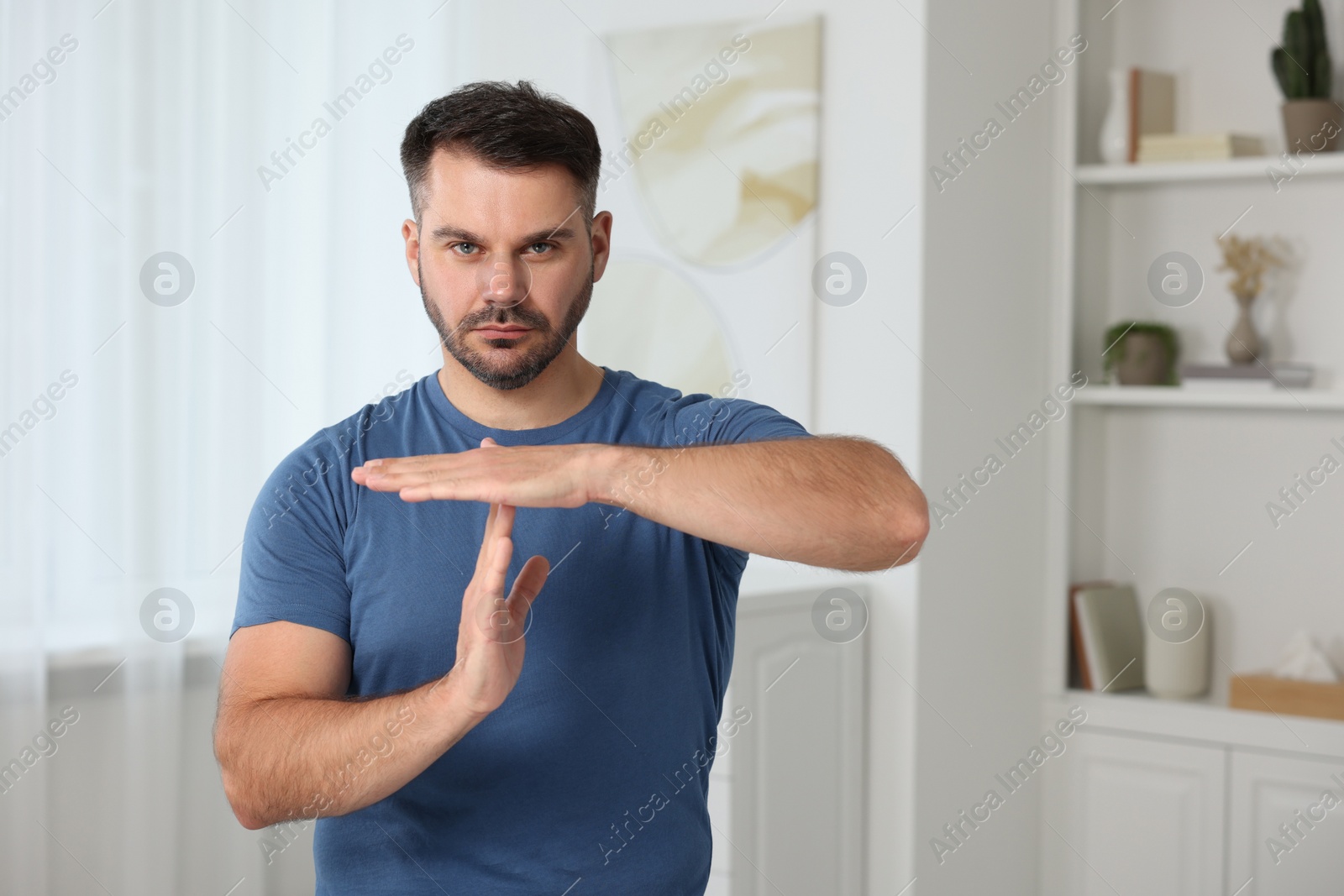 Photo of Handsome man showing time out gesture at home, space for text. Stop signal