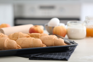 Photo of Baking tray with delicious croissants on kitchen table