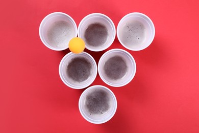 Plastic cups and ball for beer pong on red background, flat lay