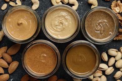 Photo of Tasty nut butters in jars and raw nuts on dark gray table, flat lay