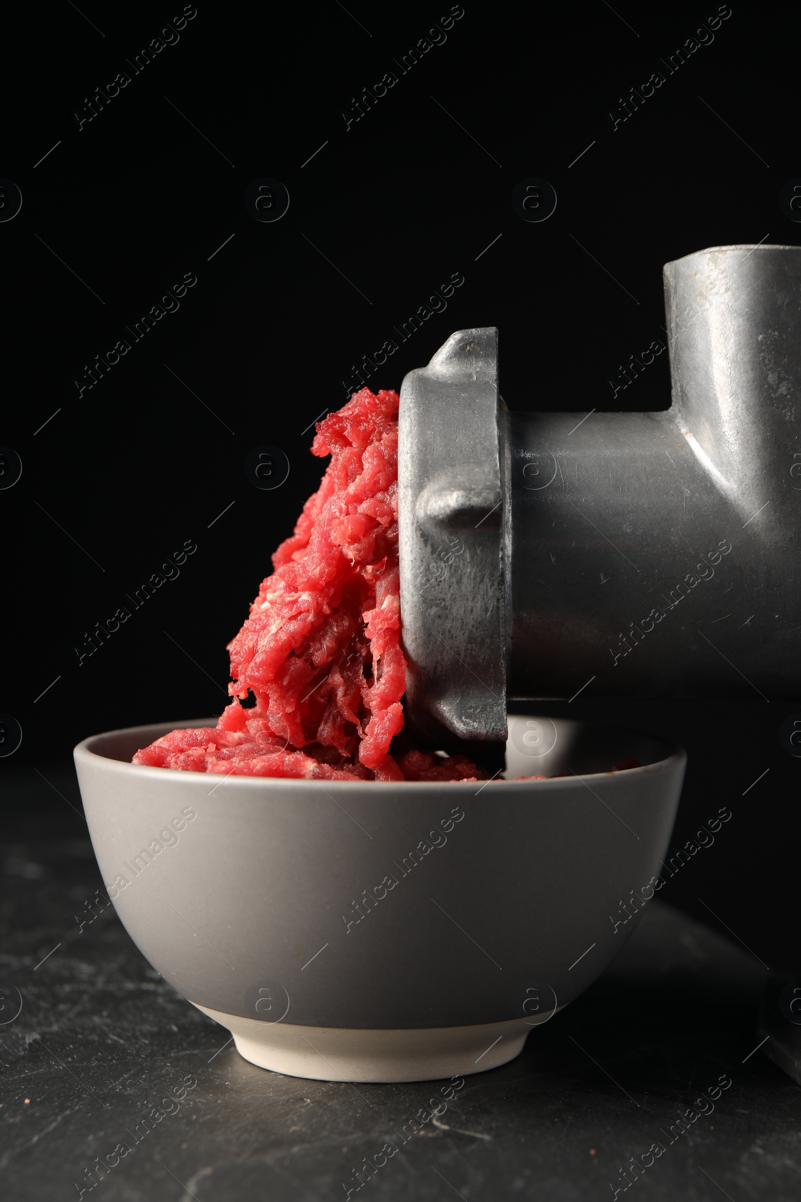 Photo of Mincing beef with metal meat grinder on dark textured table against black background, closeup