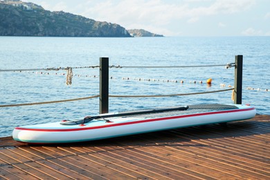 Photo of SUP board with paddle on wooden pier near sea