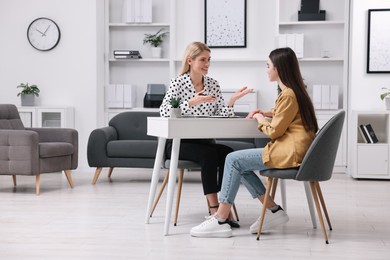 Psychologist working with teenage girl at table in office, space for text