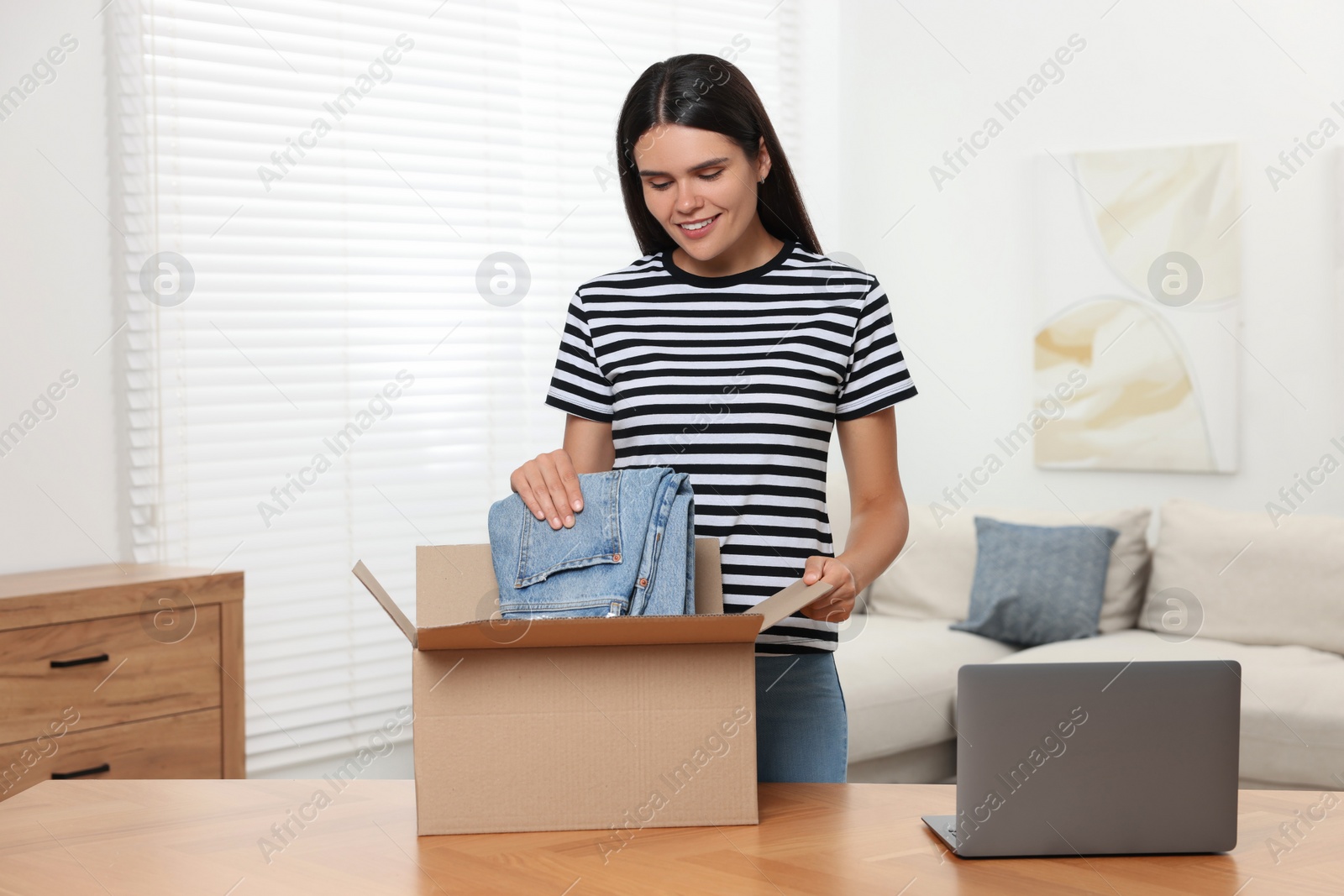 Photo of Young woman with just unpacked new jeans at wooden table indoors. Online shopping