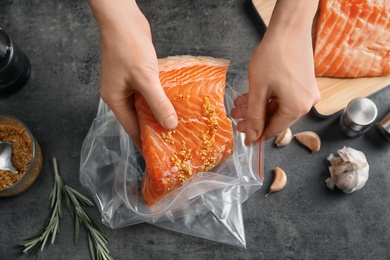 Photo of Woman putting marinated salmon fillet into plastic bag at table, top view