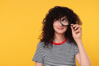 Photo of Curious young woman looking through magnifier glass on yellow background. Space for text
