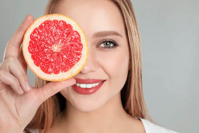 Photo of Young woman with cut grapefruit on grey background. Vitamin rich food