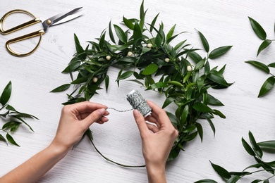 Woman making mistletoe wreath at white wooden table, top view. Traditional Christmas decor